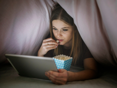 Kobieta oglada film pod koldra na laptopie
