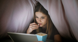 Kobieta oglada film pod koldra na laptopie