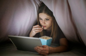 Kobieta oglada film pod koldra na laptopie