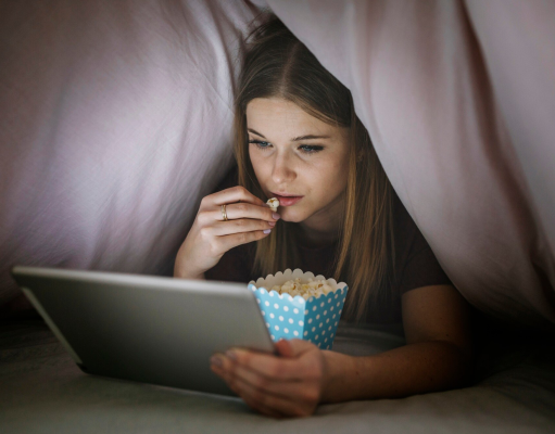 Kobieta oglada film pod koldra na laptopie