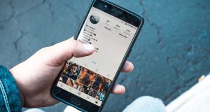 Dłoń trzymająca telefon z otwartą aplikacją social media na ekranie.