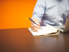 Jak napisać biznesplan dla małej firmy Osoba pisząca notatki w notesie przy laptopie podczas planowania biznesu.