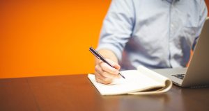 Jak napisać biznesplan dla małej firmy Osoba pisząca notatki w notesie przy laptopie podczas planowania biznesu.