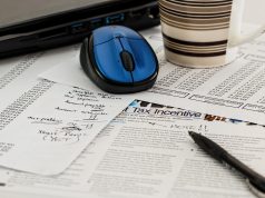 Dokumenty podatkowe z napisem Tax Incentive, długopis, mysz komputerowa i kubek kawy na biurku.