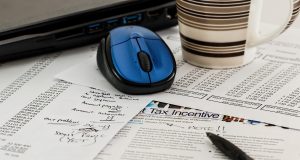 Jakie formy opodatkowania wybrać dla jednoosobowej działalności gospodarczej Dokumenty podatkowe z napisem Tax Incentive, długopis, mysz komputerowa i kubek kawy na biurku.