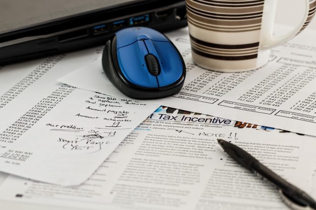 Dokumenty podatkowe z napisem Tax Incentive, długopis, mysz komputerowa i kubek kawy na biurku.
